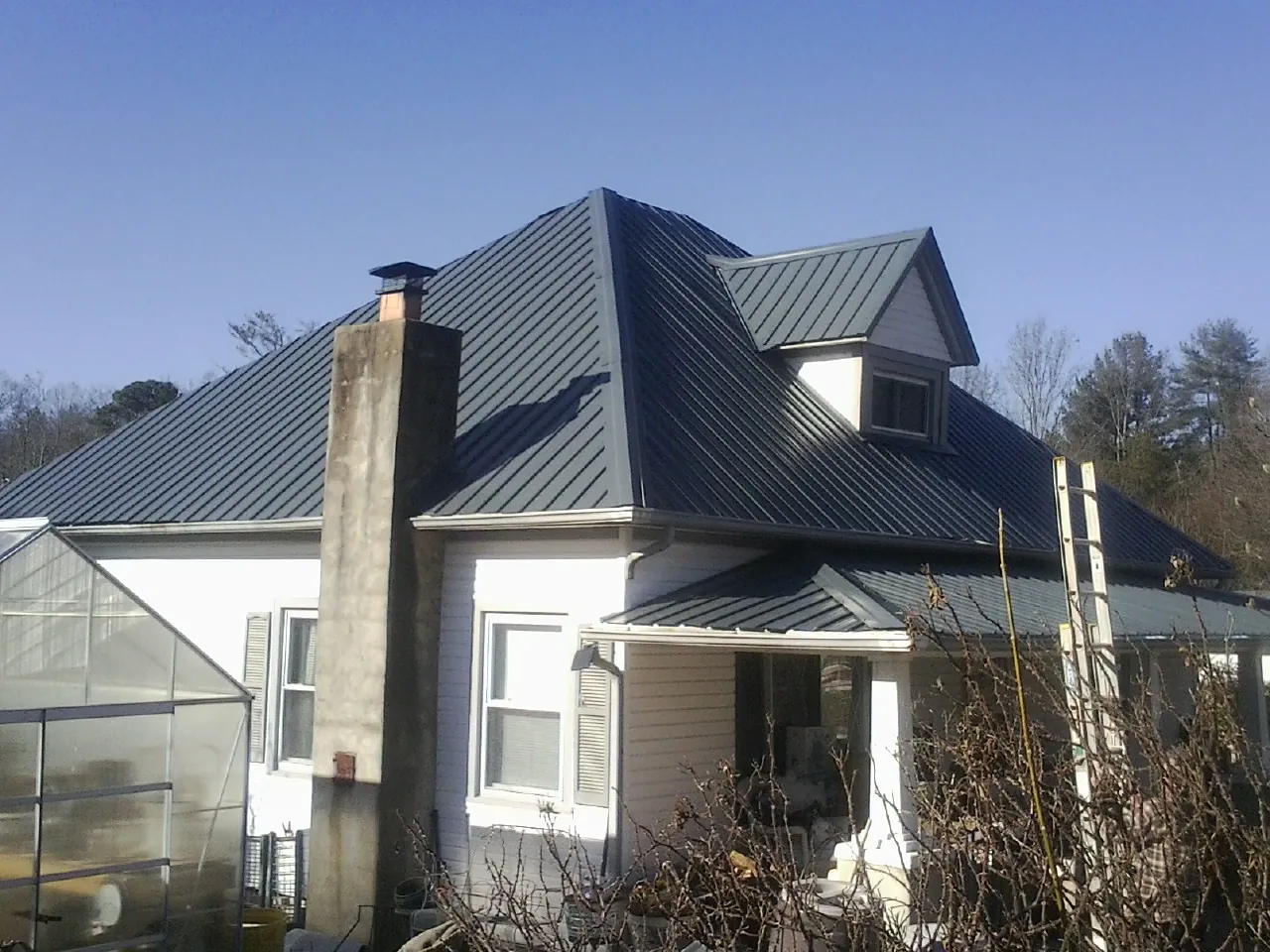 Dark blue standing seam metal roof on a white farmhouse with dormer — Slate & Tile Roof Repair by Roofing Brothers in Loysburg