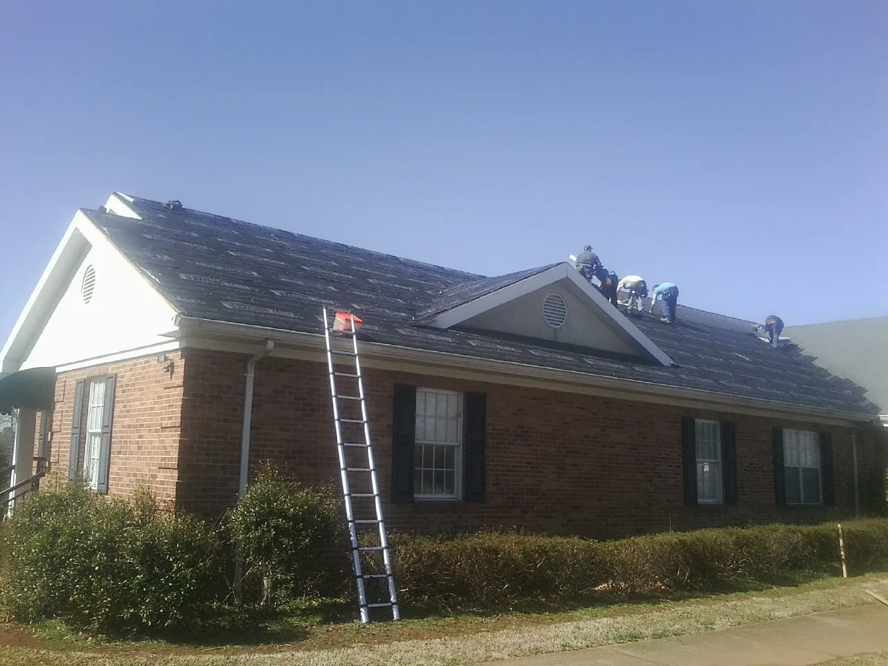 Crew tearing shingles off a brick ranch roof with a ladder set — Metal Roof Repair work by our crew in Loysburg