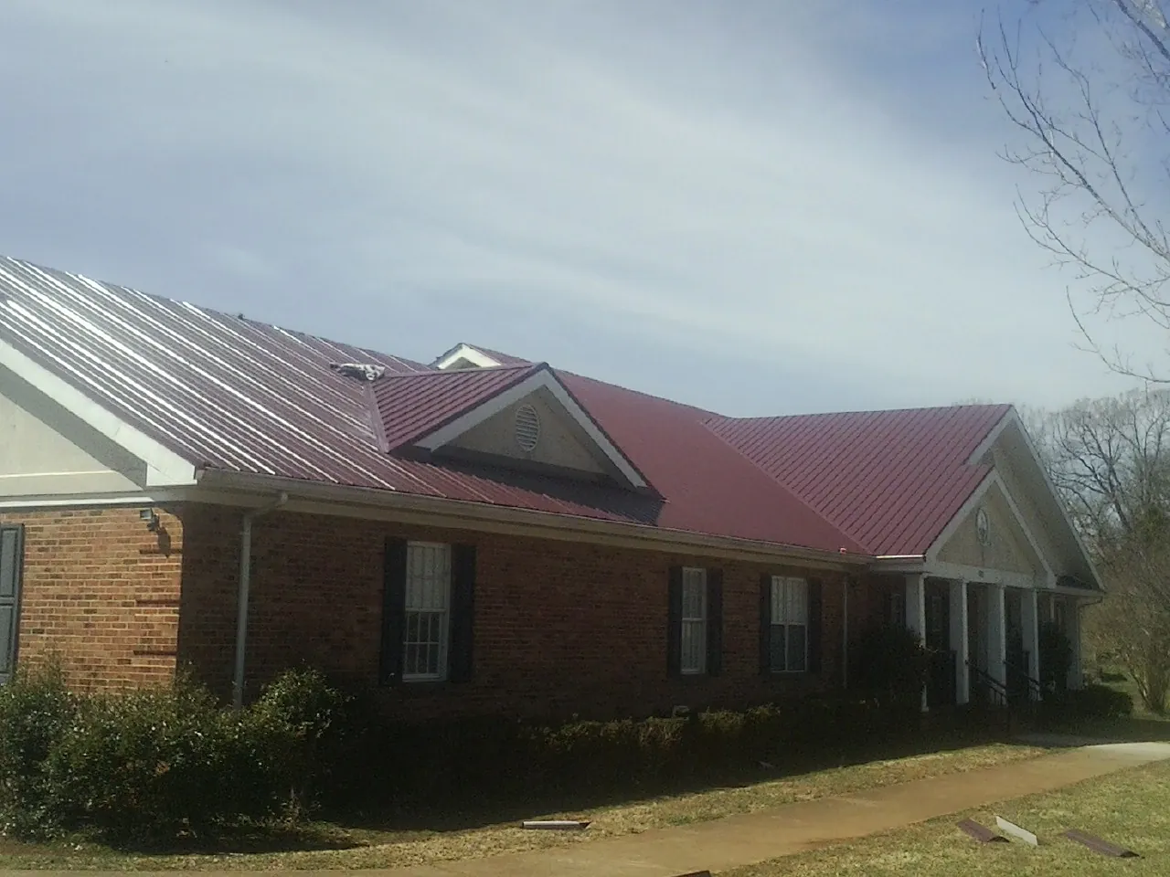 Red metal roof with gabled entries on a long brick building, from a Hail Damage Roof Repair job in Loysburg