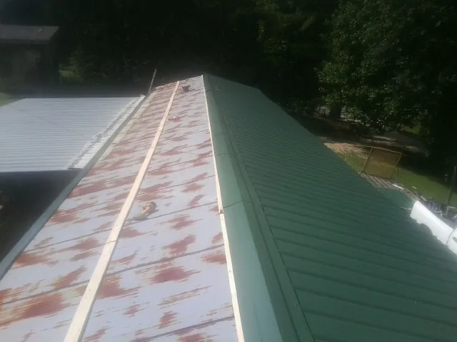Old rusted panels beside newly installed green metal roofing — Wind Damage Roof Repair by Roofing Brothers in Loysburg