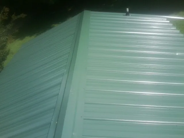 New green metal panels meeting at the ridge of a roof — Flat Roof Repair work by our crew in Loysburg
