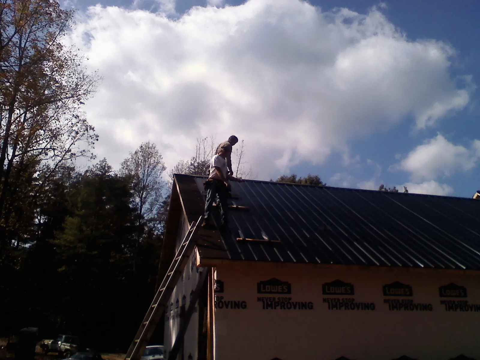 Roofer fastening dark metal panels high against a cloudy sky, from a Roof Inspection job in Loysburg