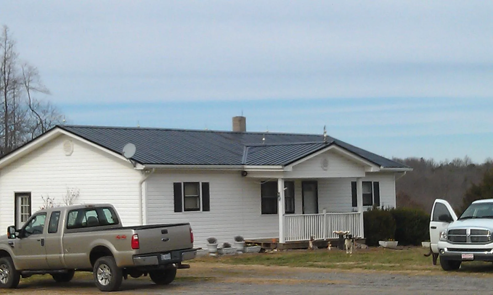 Finished dark metal roof on a white ranch home with work trucks parked in Loysburg
