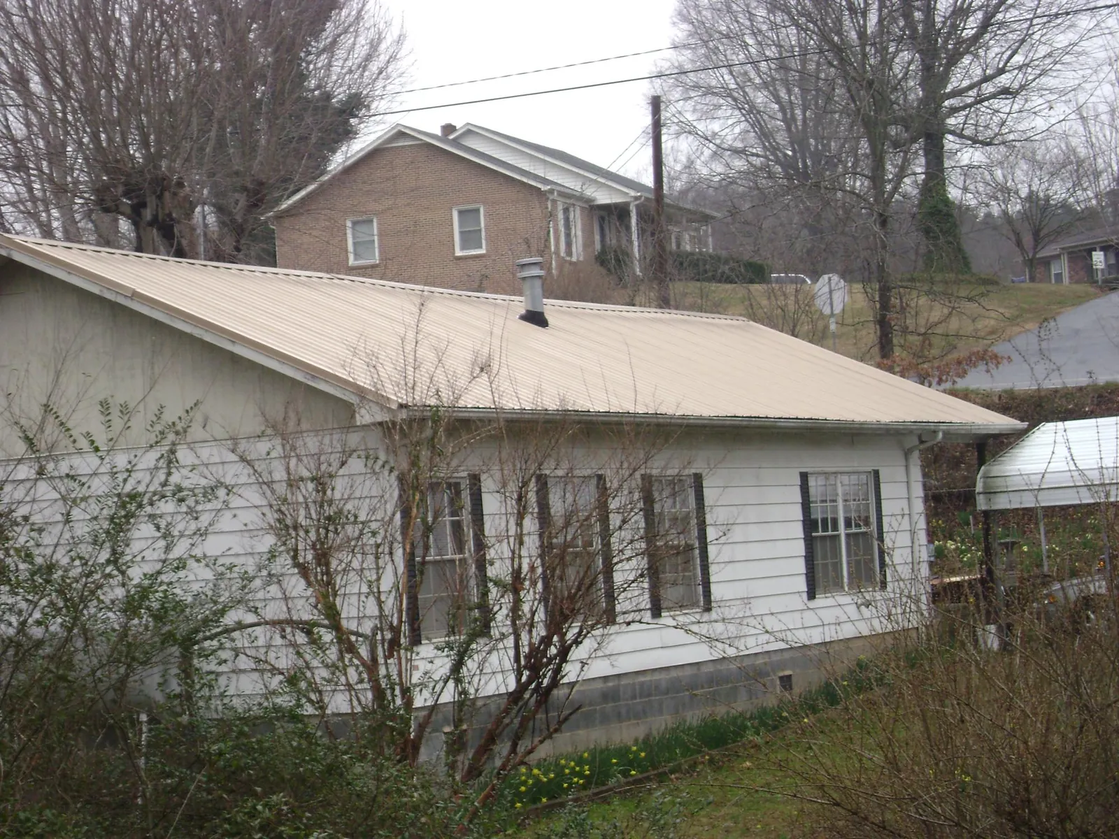 Tan metal roof on a white sided house set into a hillside — Commercial Roofing by Roofing Brothers in Loysburg